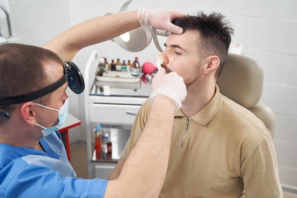 Man sitting in a dentist's chair with a mask on, while a dentist wearing a mask