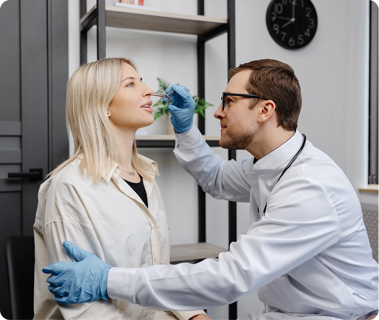Woman sitting in a chair with a doctor wearing a stethoscope and gloves examining her teeth