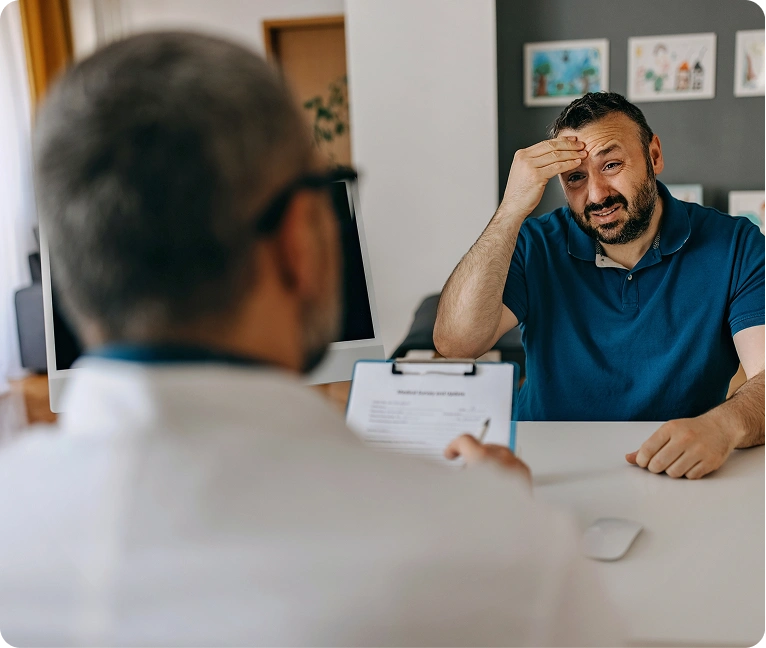 Man sitting at a desk with his head in his hands, looking at a doctor who is holding a paper