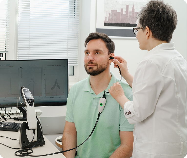 Man sitting in a chair with a stethoscope in his ear, while a woman stands beside him