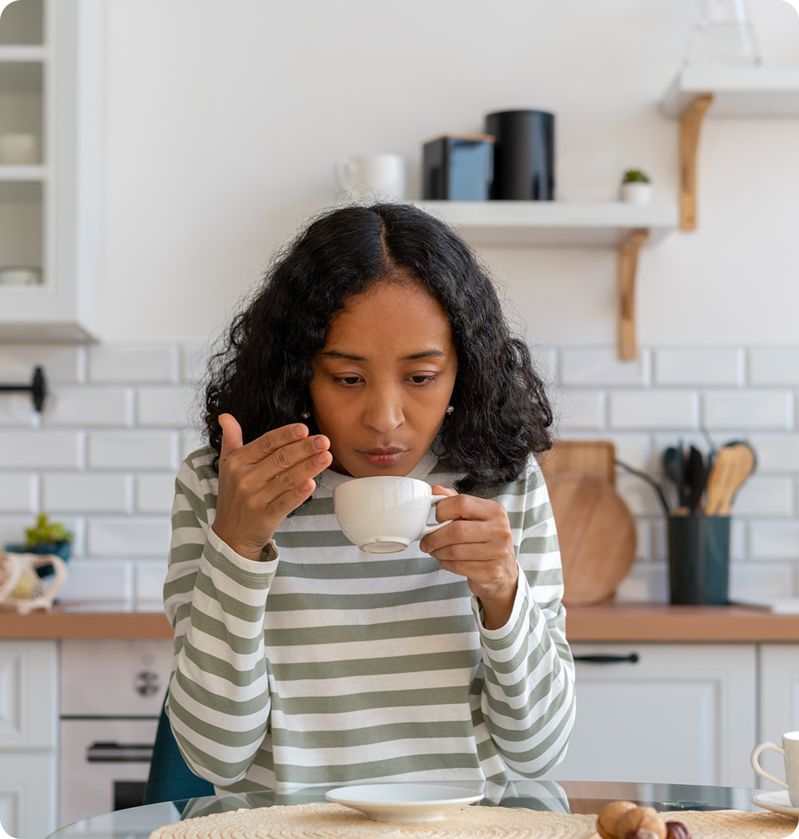 Woman sitting at a kitchen table, holding a cup of coffee in her hands