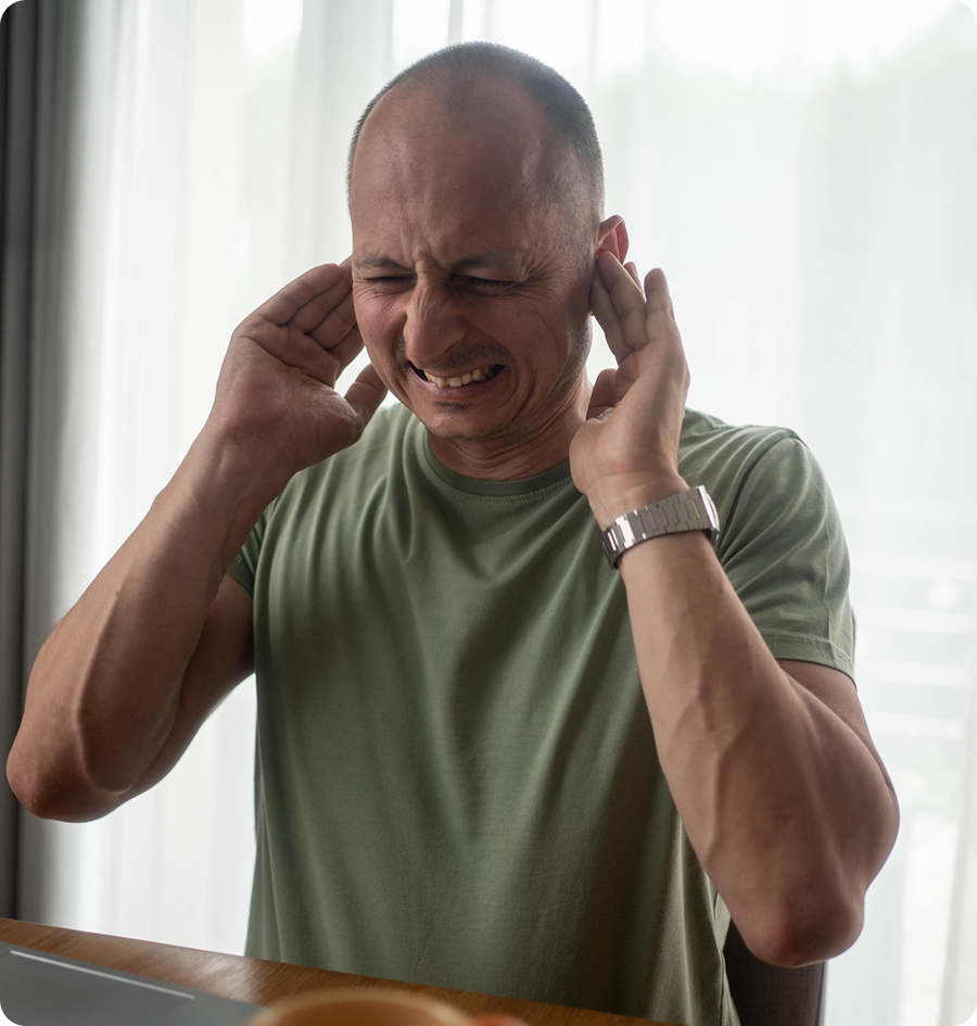Man sitting at a table with his hands on his ears, wearing a t-shirt and a watch