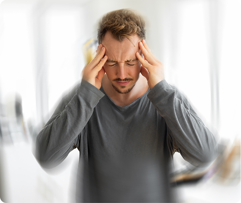 Man wearing a t-shirt, holding his head in his hands in a gesture of distress, with a blurred background