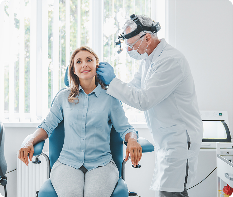 Woman sitting in a dentist's chair with a man standing beside her, wearing a mask and glasses