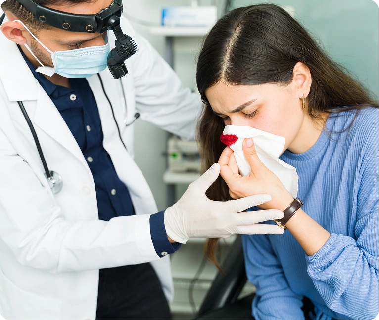 Woman sitting in a chair with a tissue in her mouth, while a doctor wearing a mask, stethoscope
