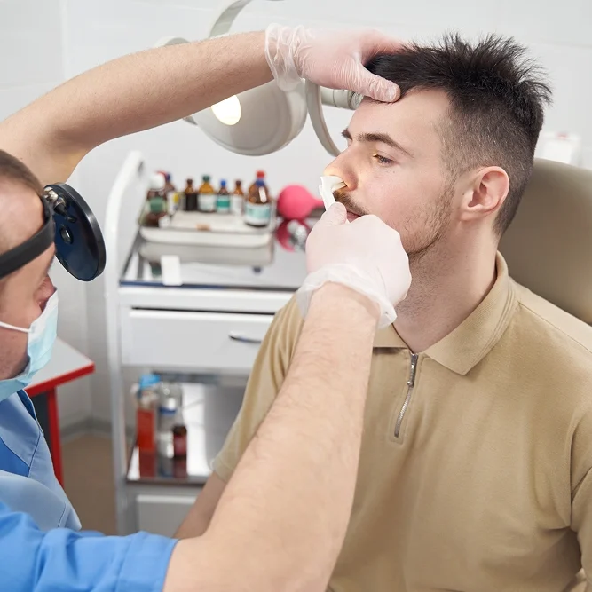 Man sitting in a dentist's chair with a mask on, while a dentist wearing a mask