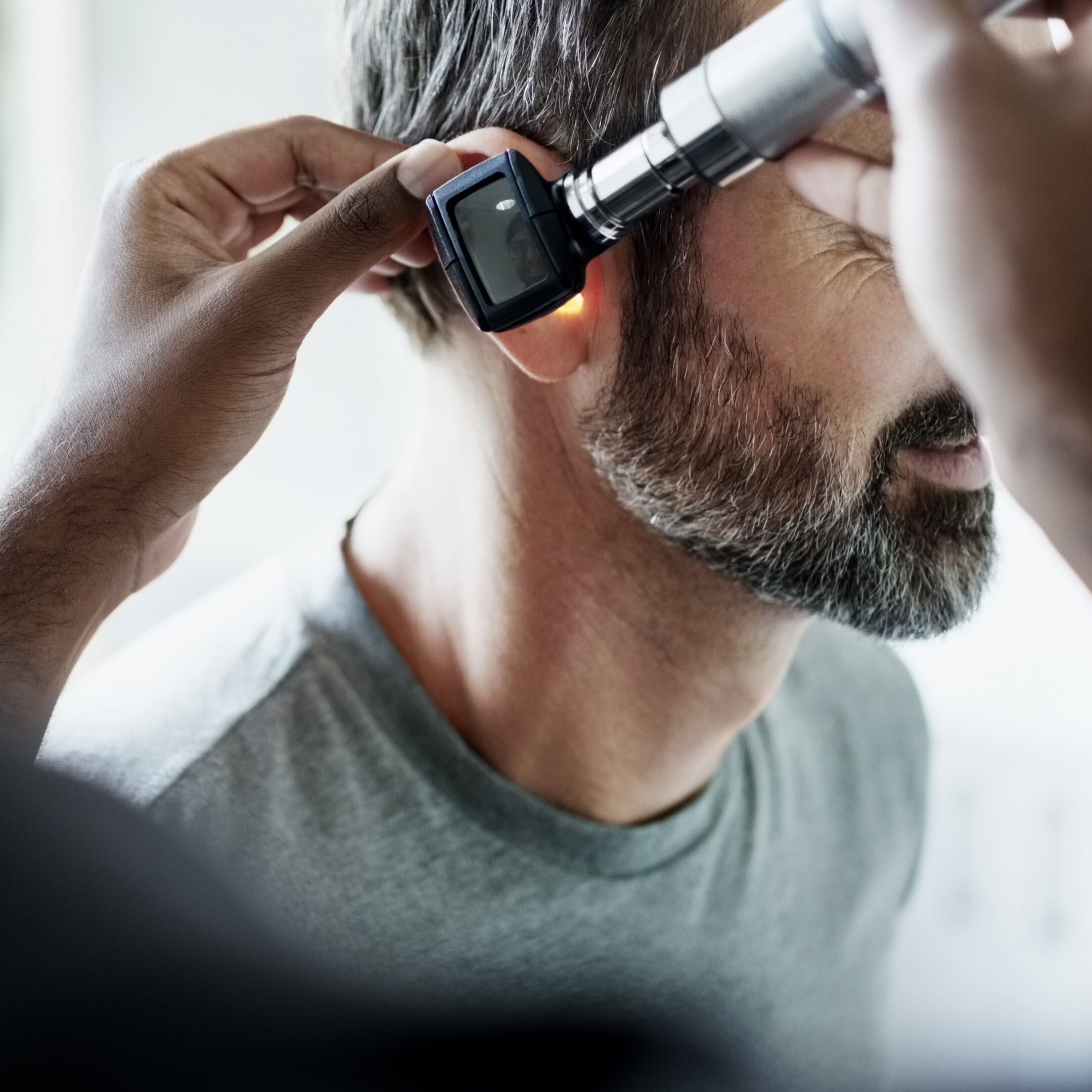 Over the shoulder view of doctor holding otoscope and examining patient's ear inside of clinic examination room during a checkup