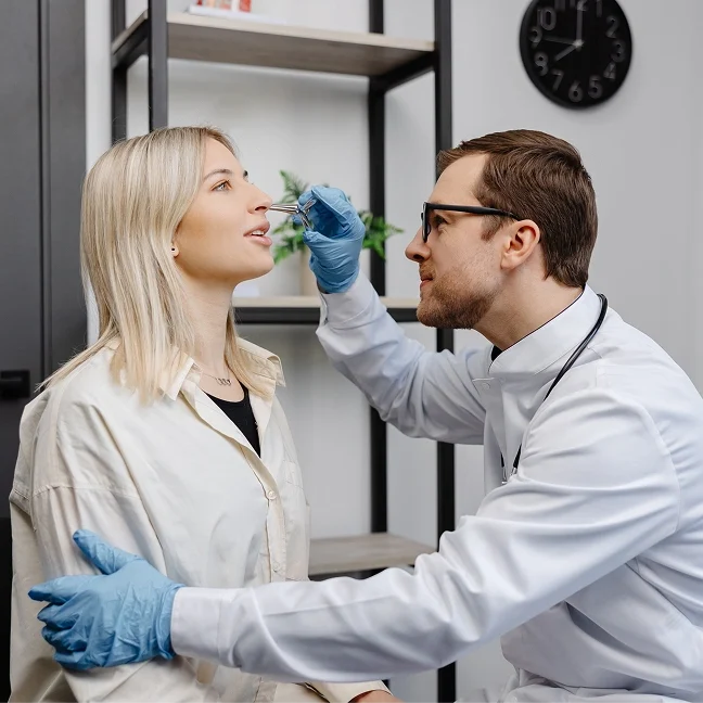 Woman sitting in a chair with a doctor wearing a stethoscope and gloves examining her teeth