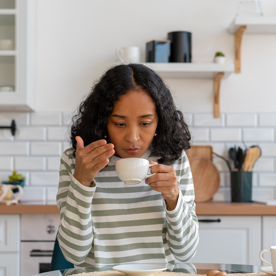 Woman sitting at a kitchen table, holding a cup of coffee in her hands