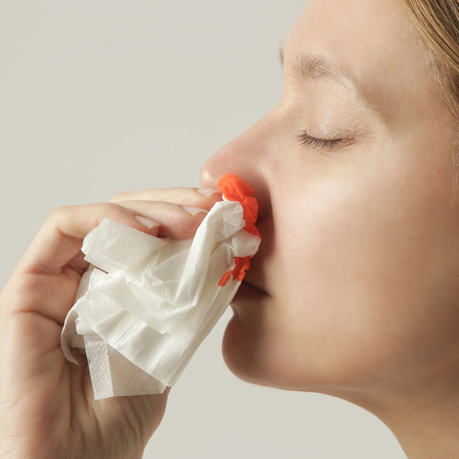 Woman blowing her nose with a tissue in her hand against a white background