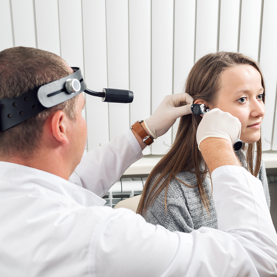 Woman getting her ear examined by a doctor wearing a coat and a watch