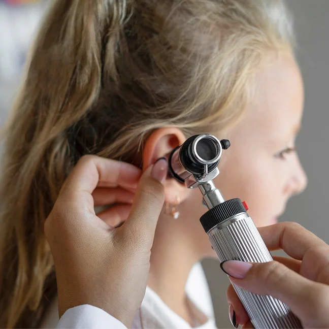 Little girl getting her ear examined by a doctor, holding an otoscope in her hand