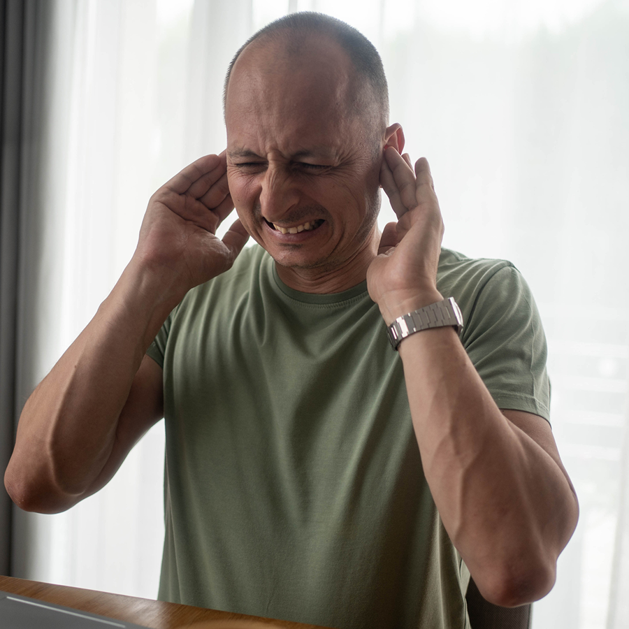 Man sitting at a table with his hands on his ears, wearing a t-shirt and a watch