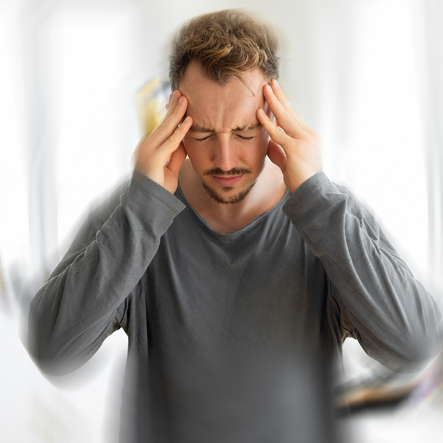Man wearing a t-shirt, holding his head in pain, with a blurred background