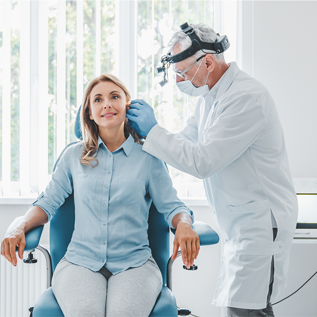 Woman sitting in a dentist's chair with a man standing beside her, wearing a mask and glasses