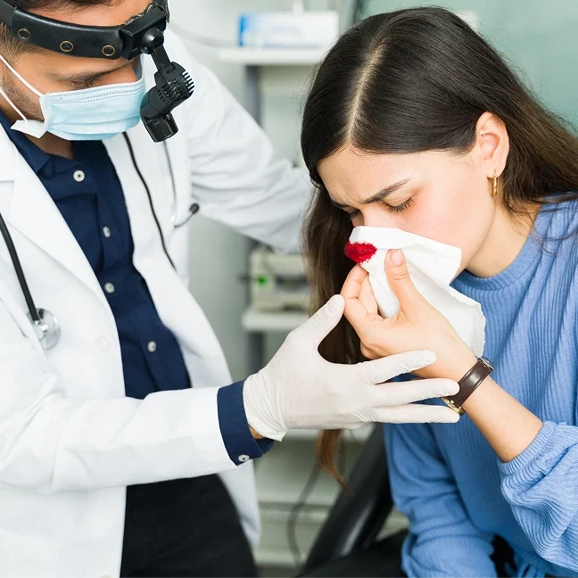 Woman sitting in a chair with a tissue in her mouth, while a doctor wearing a mask, stethoscope